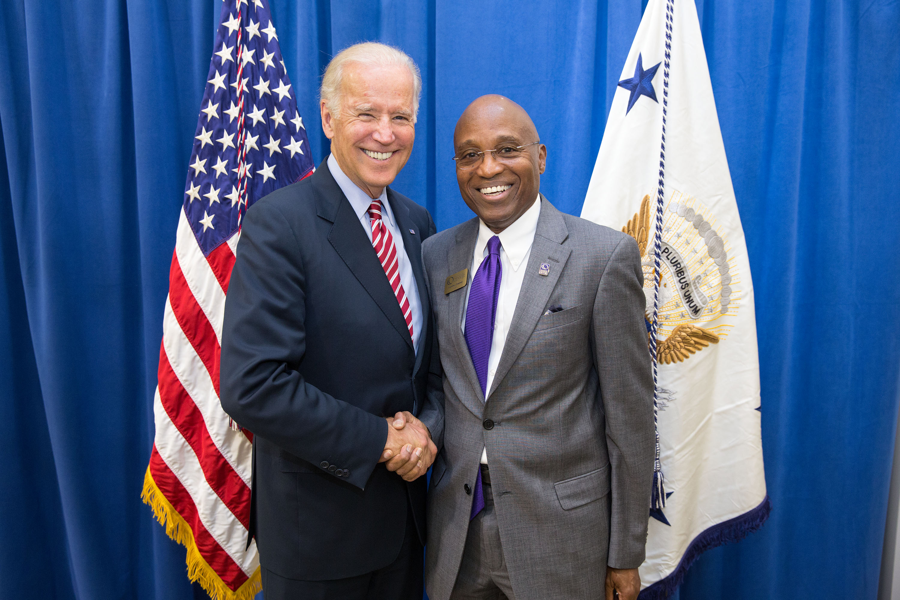 two men in suits shaking hands with American flag in background