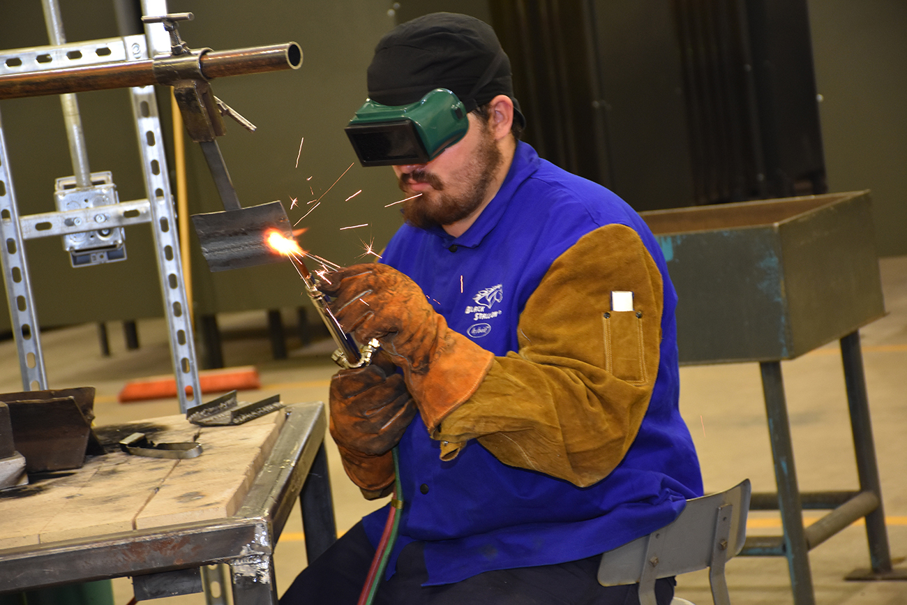 man welding while wearing protective goggles and gloves