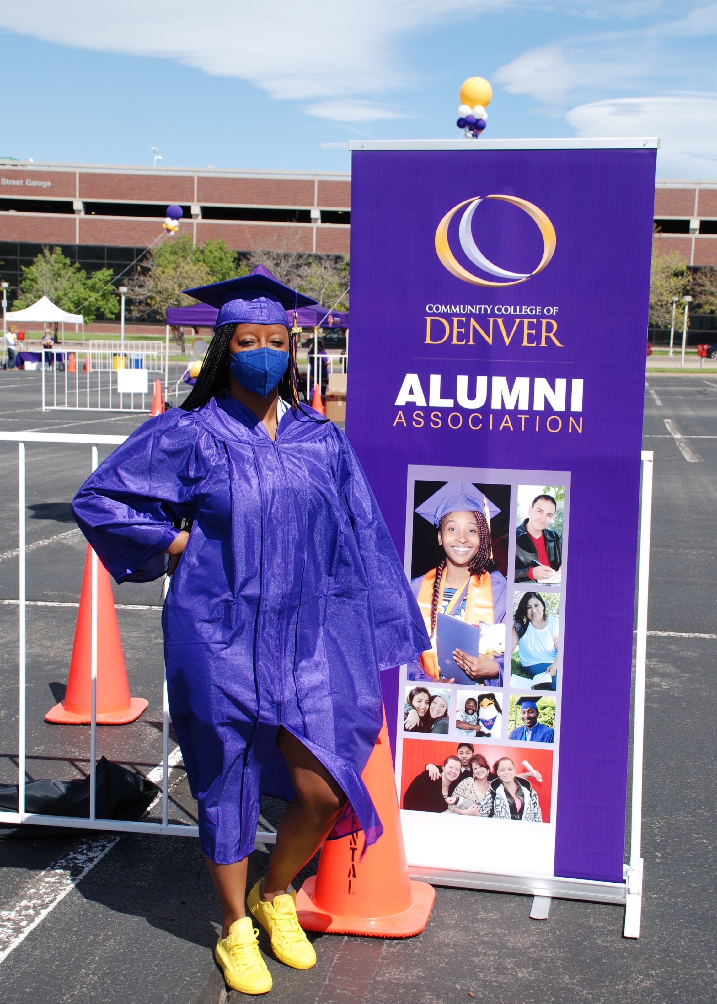 Student in cap and gown posing next to CCD Alumni Association banner 