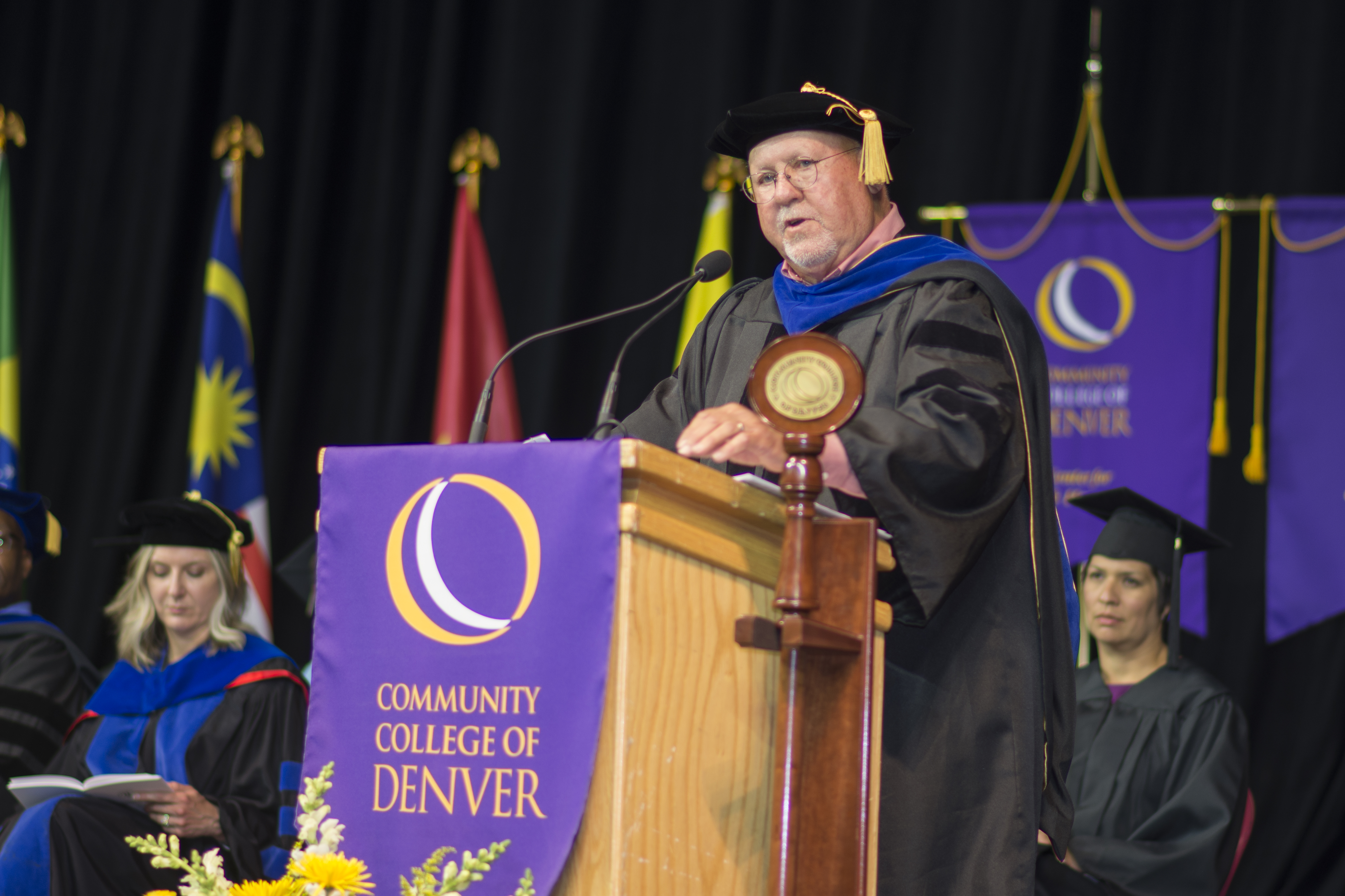man in a black cap and gown giving a keynote commencement address