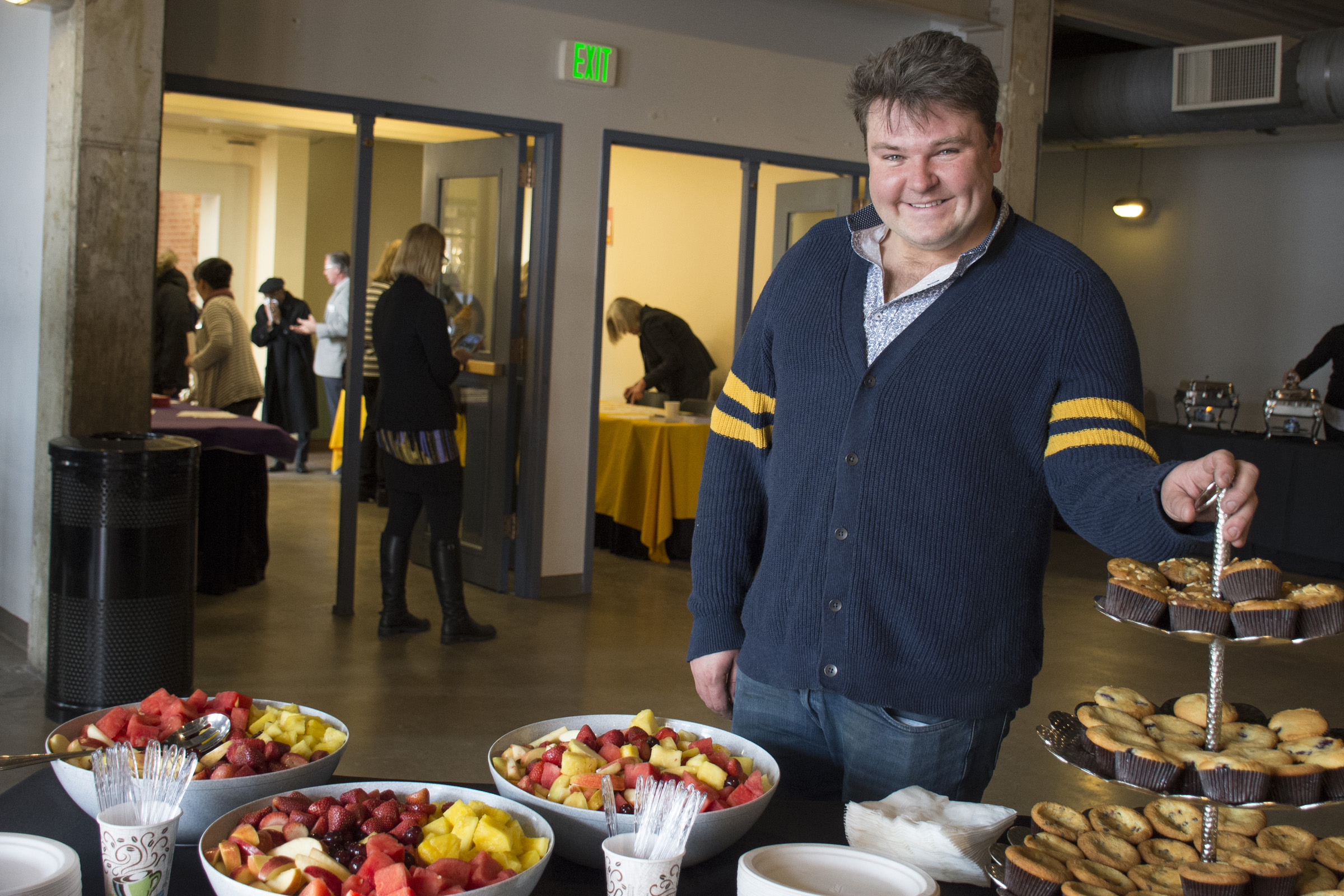 CCD Alumnus David Bondarchuck of Scratch Catering caterer stands next to table of breakfast food