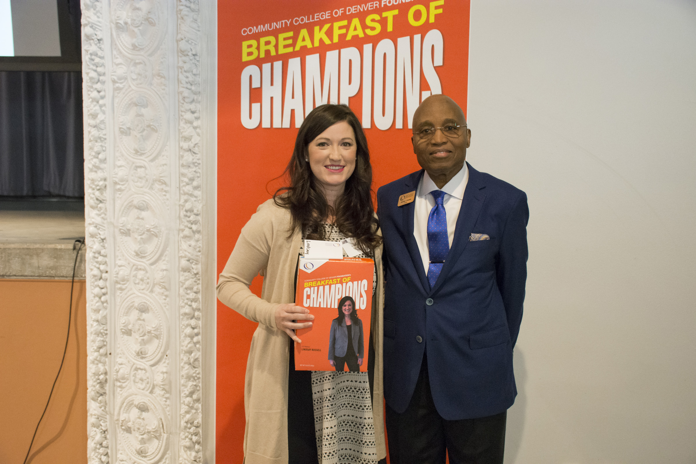 CCD Dental Hygiene Alumna Lindsay Russell with CCD President Everette Freeman woman holding a Breakfast of Champions cereal box next to man in suit