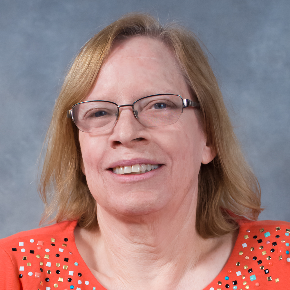 Woman with glasses wearing an orange shirt smiling.