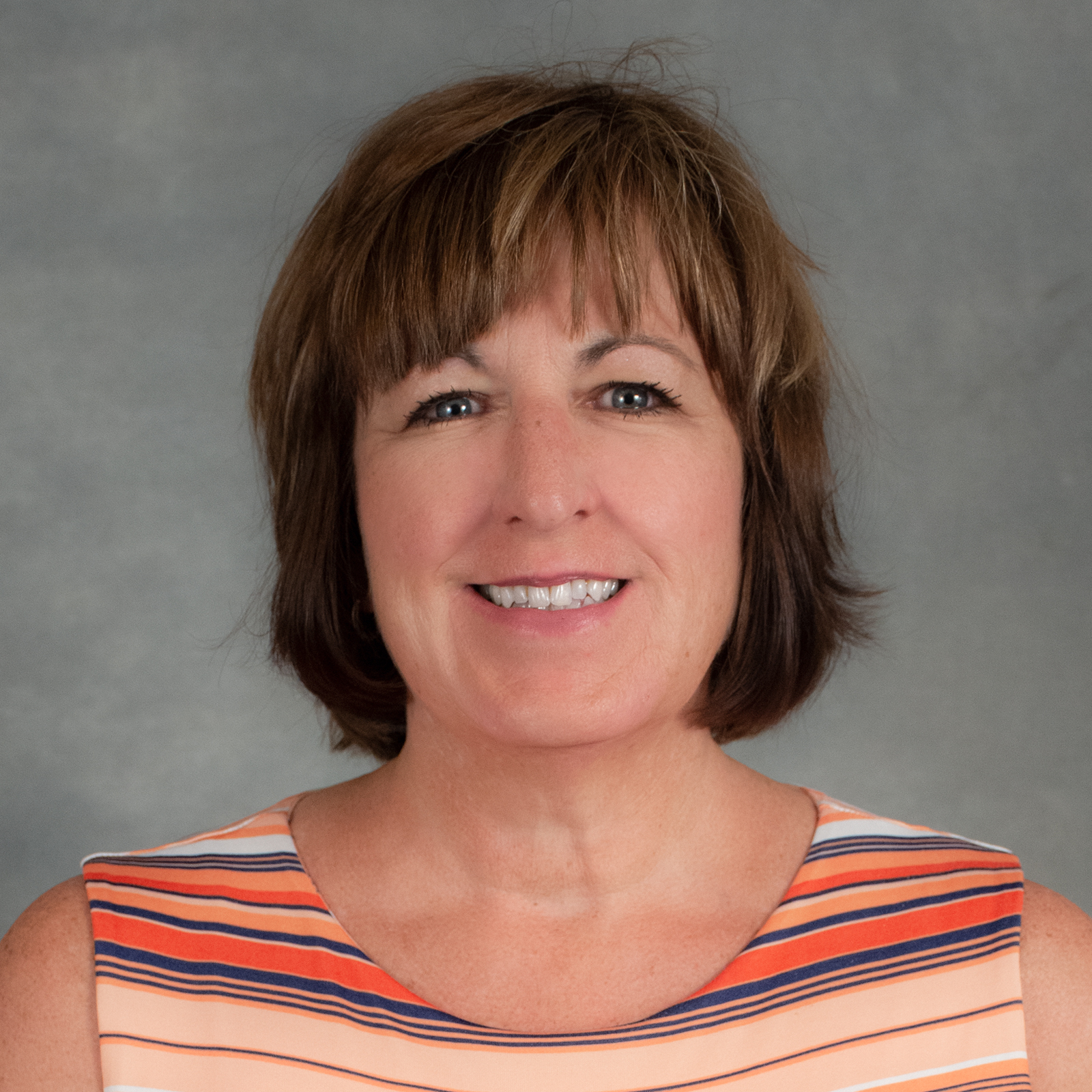 Smiling person with short brown bob with bangs wearing multi-colored striped top