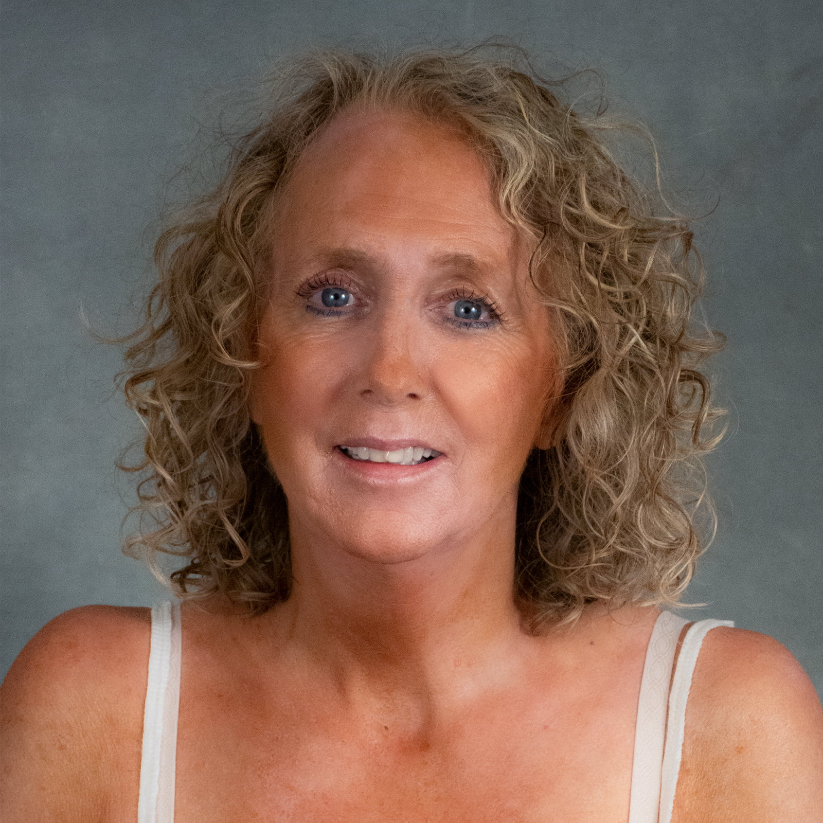 Woman with blond curly hair, wearing white sleeveless top