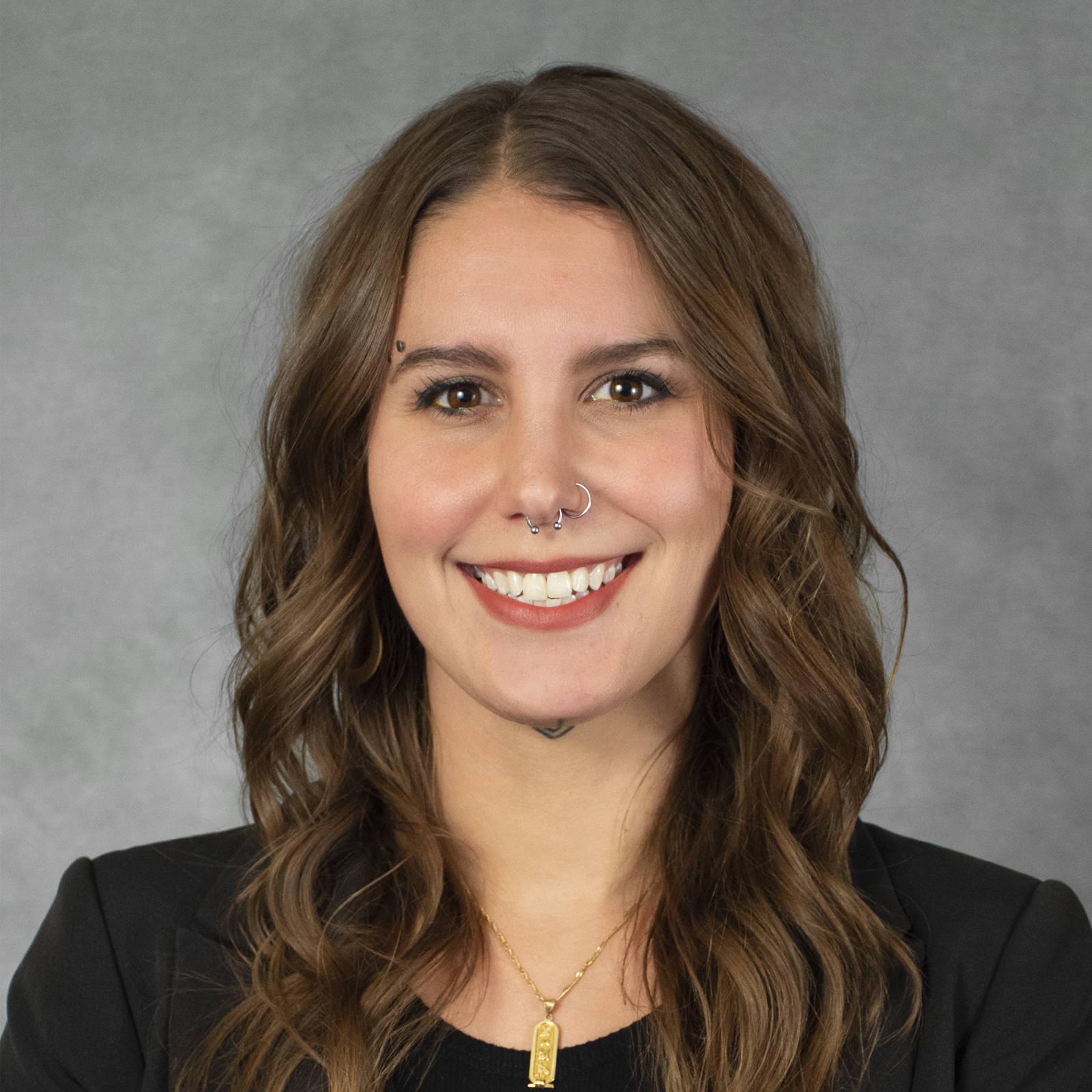 Smiling woman with shoulder-length wavy brown hair wearing a gold necklace and black top