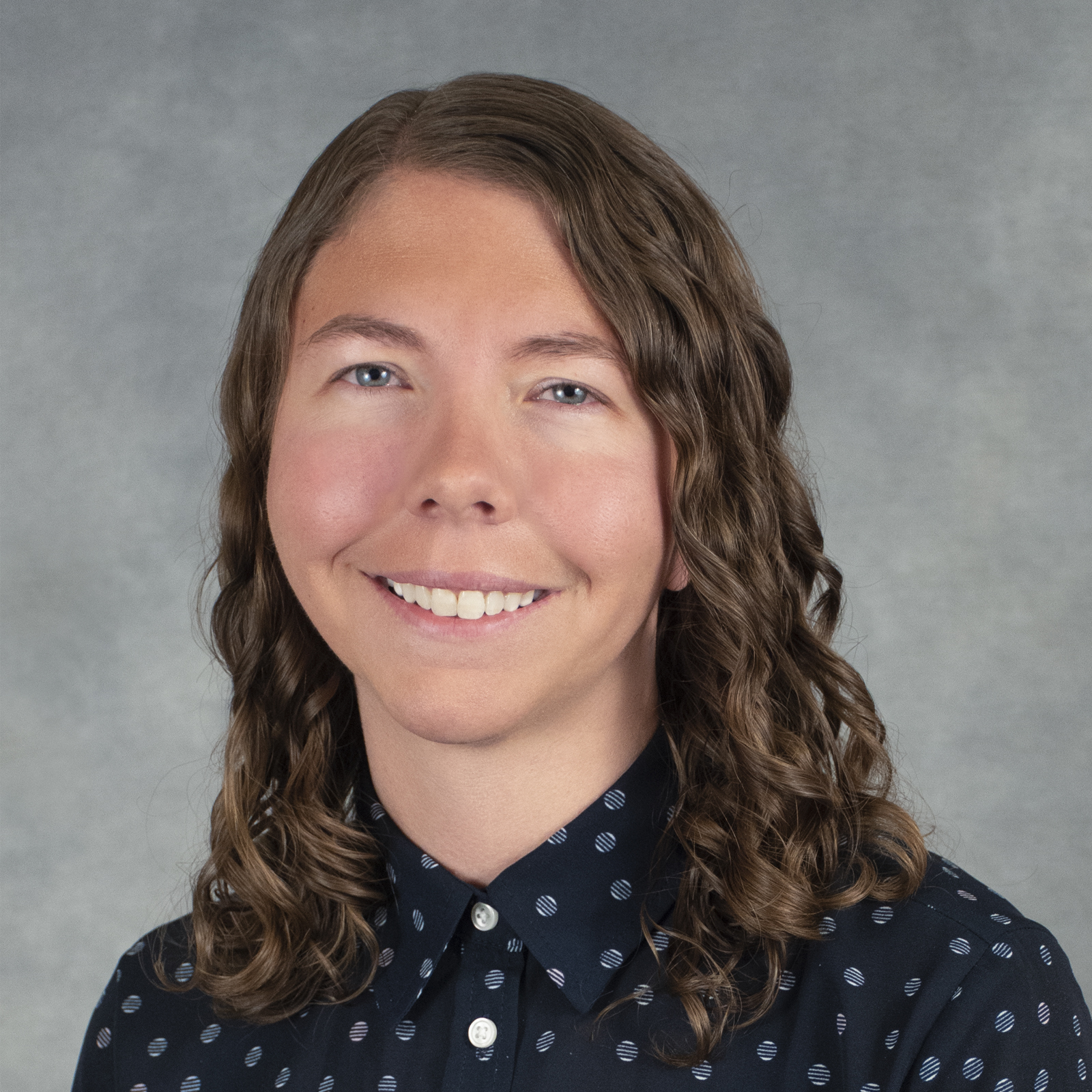 Smiling person with medium length wavy brown hair wearing a black print shirt