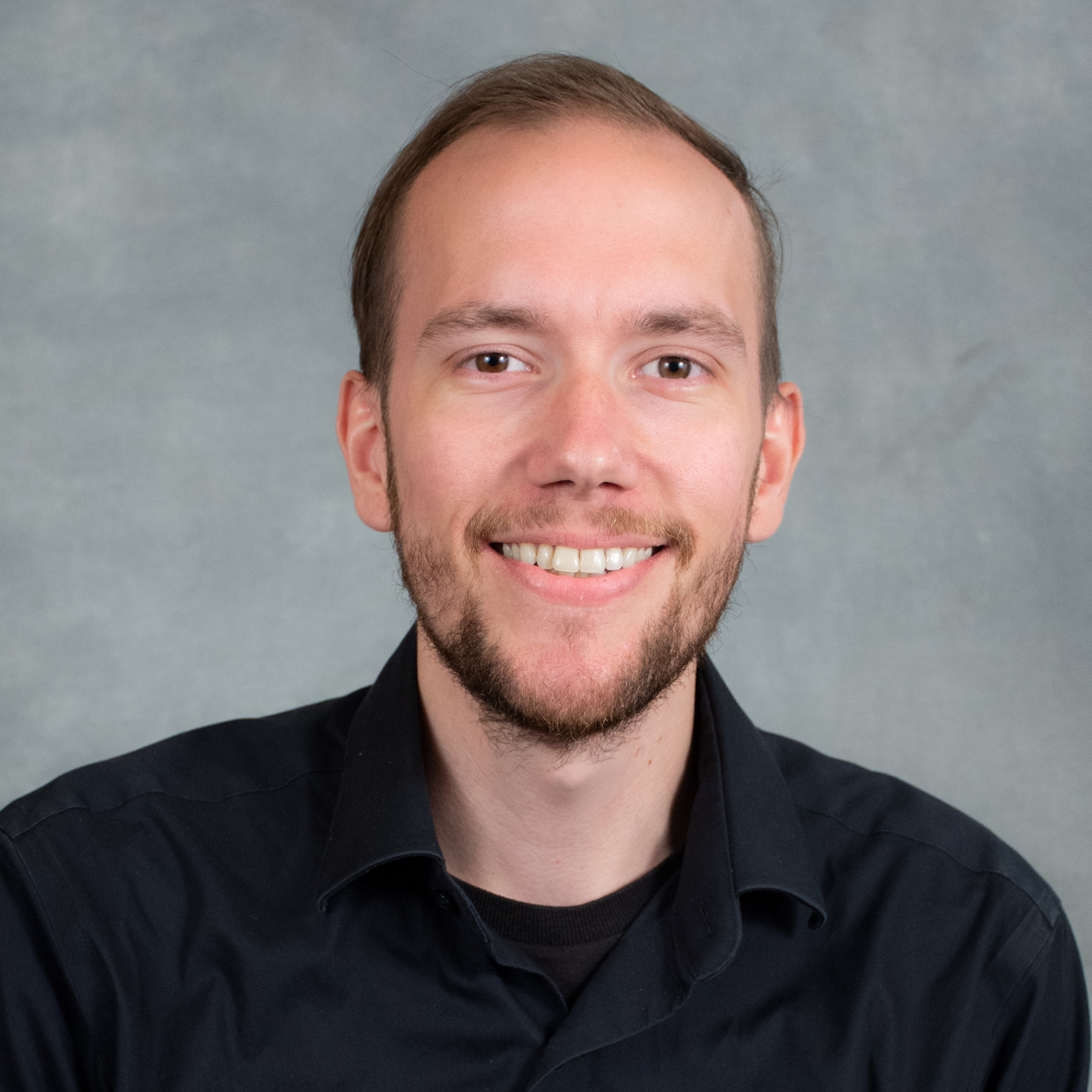 Smiling man with short brown hair and beard wearing a black shirt