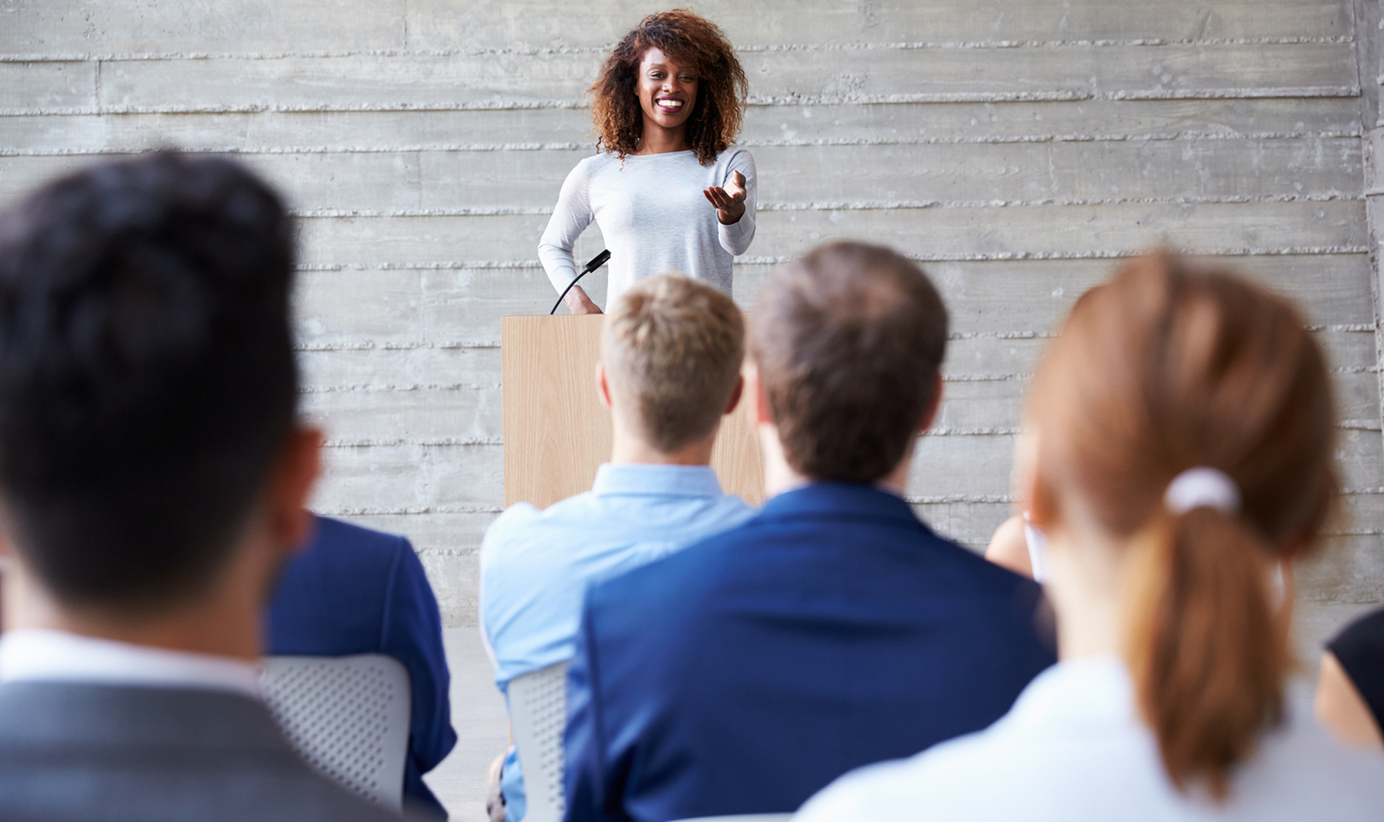 Smiling woman standing at podium giving speech to a seated audience.