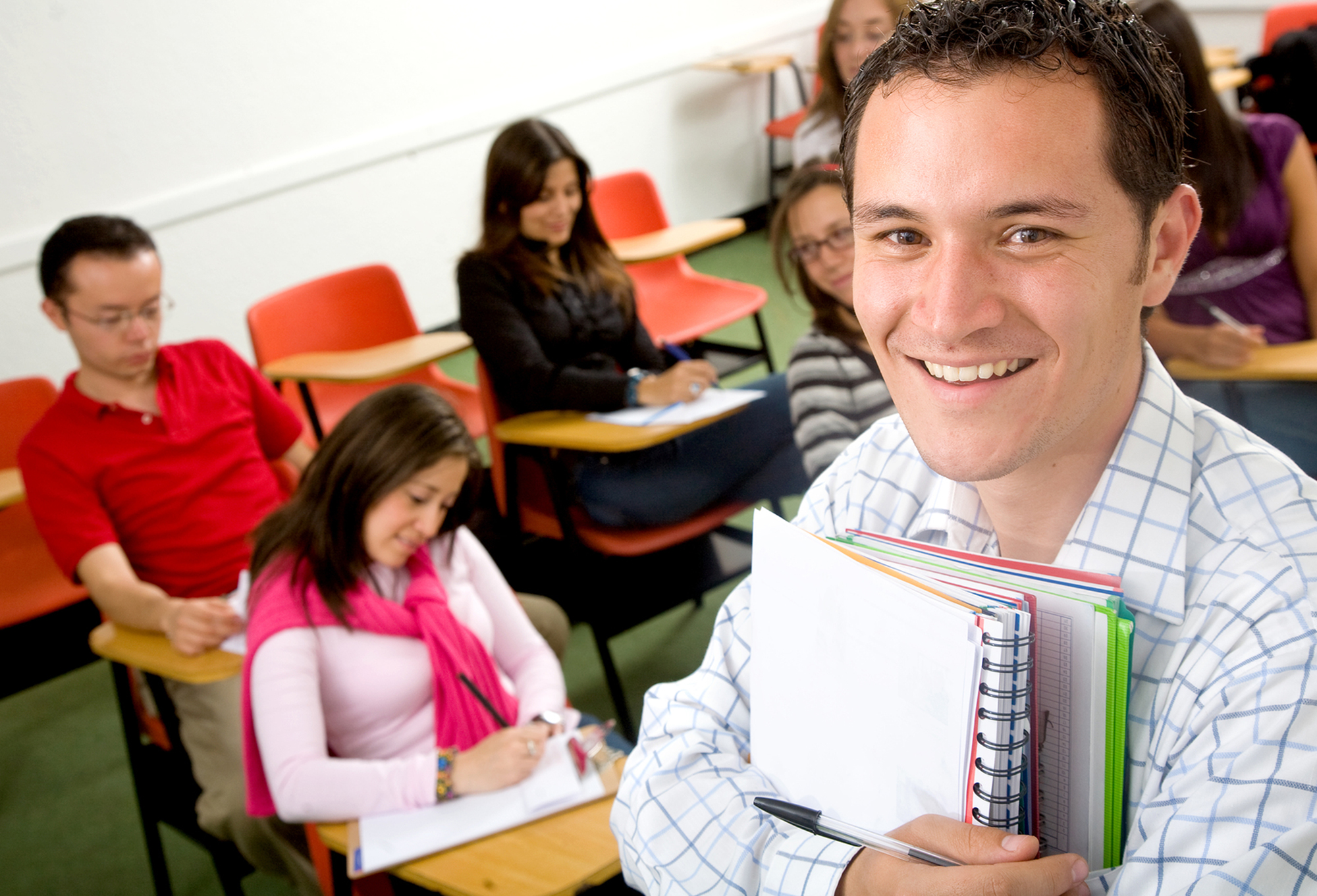 Male student holding notebooks in front of classoom