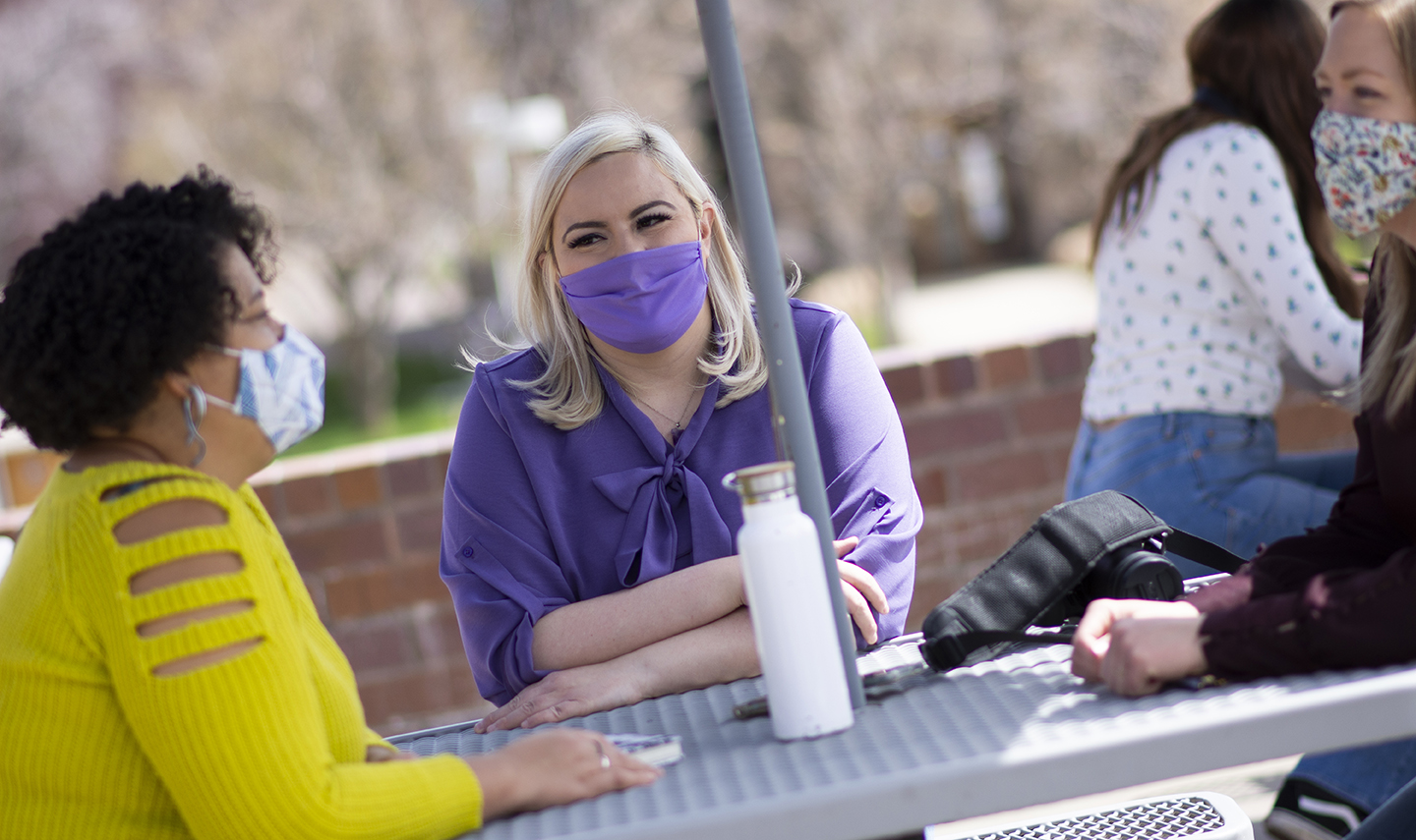 Three students at outdoor table wearing masks.