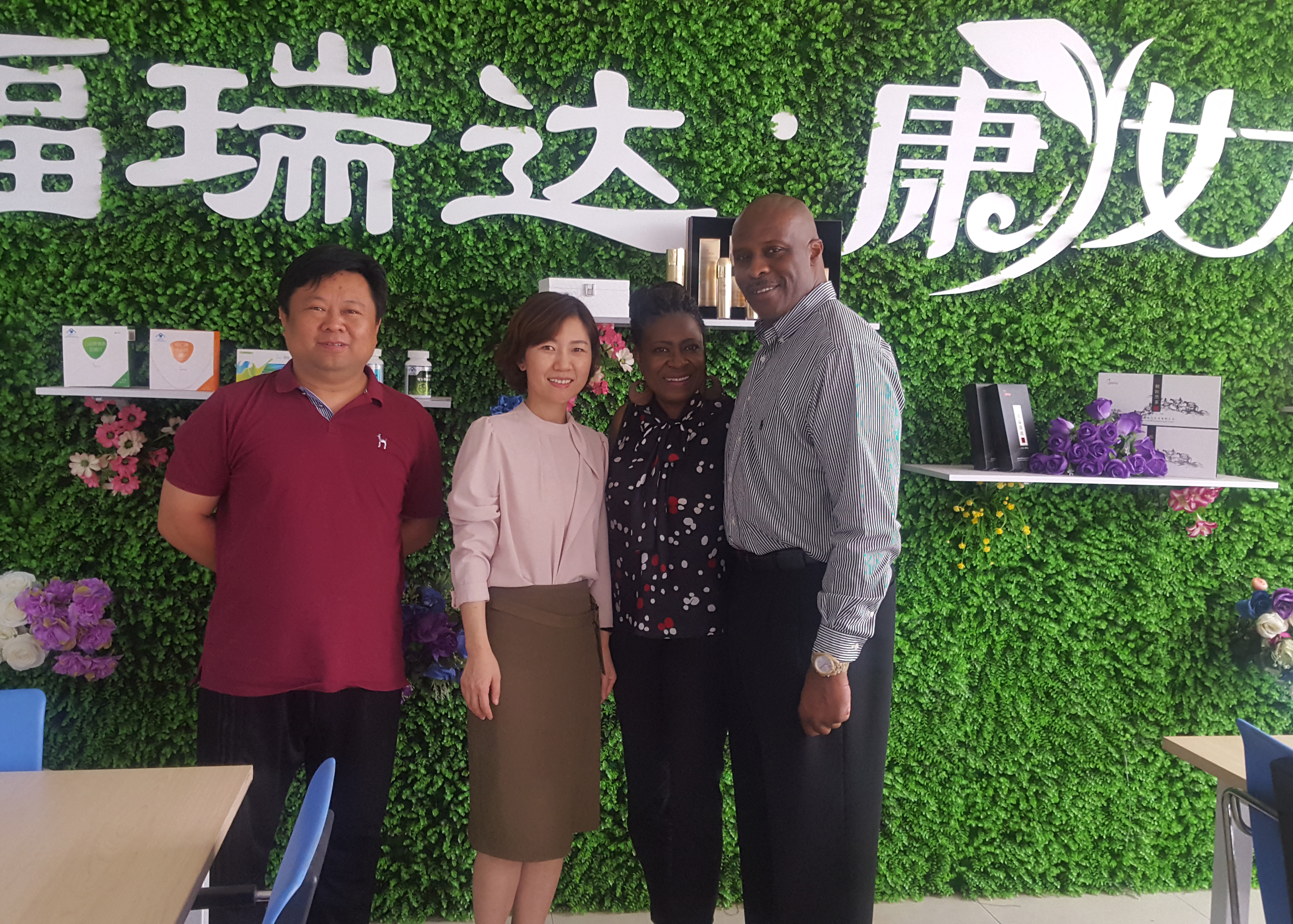 two couples standing in front of a green wall with Chinese writing on it