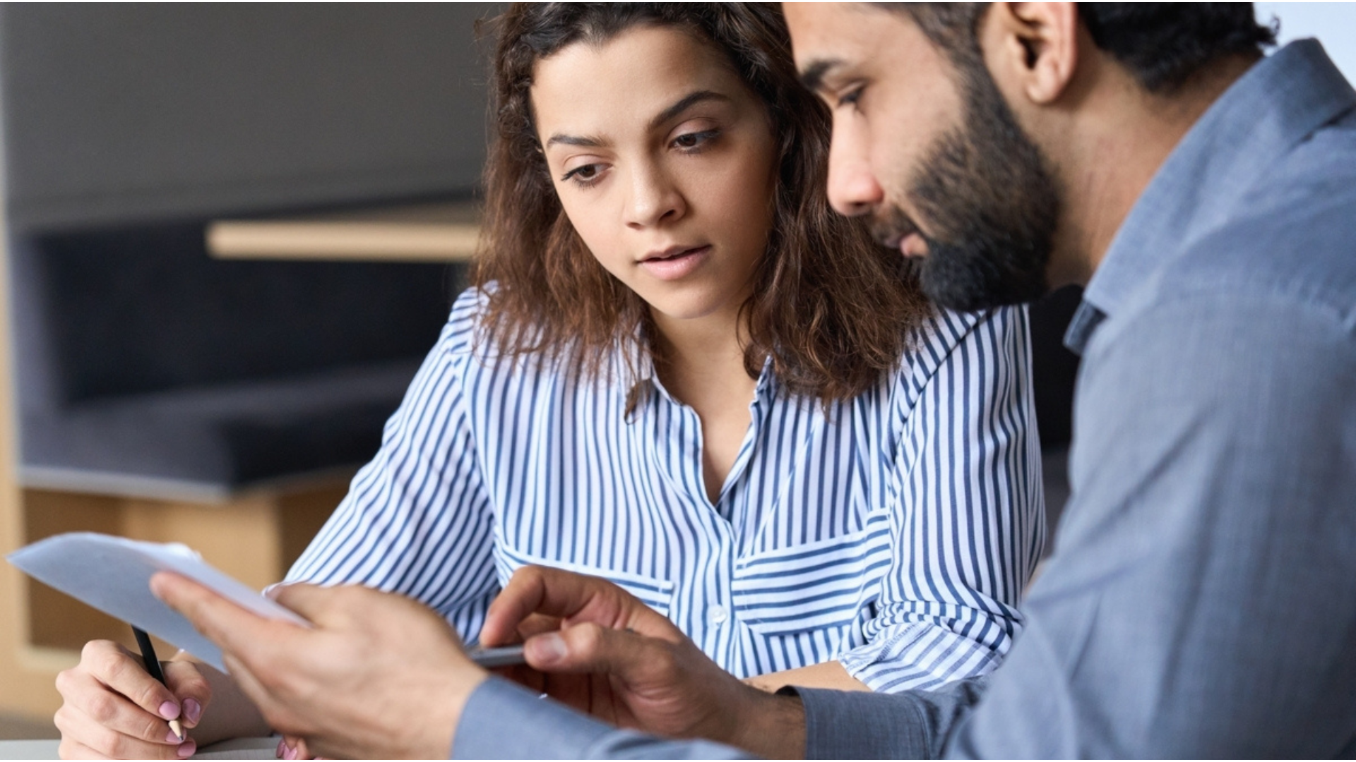image of two people meeting and reading a paper. The women is in a striped shirt, while the bearded man is in a gray shirt 