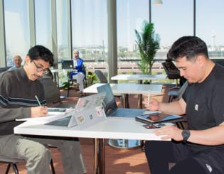 Students sitting at a tables on their laptops and iPads.