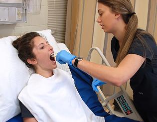 2 individuals in a medical setting, one on a hospital bed and one conducting a health-check up