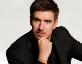white man sitting with one hand on his chin wearing a black shirt