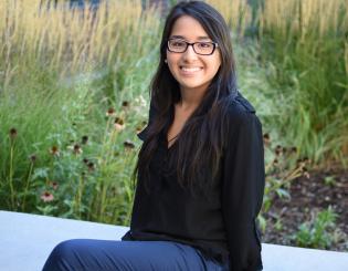 smiling student with glasses sits outside
