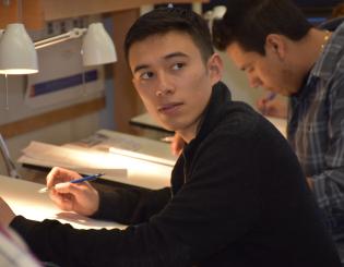 young man at a drafting table looking over his shouler