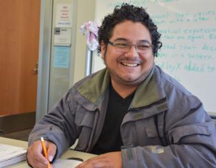 young male seated and holding a pencil smiling