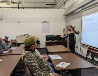 woman in a mask at a white board teaching to a group of ESL students
