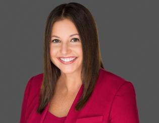 Hispanic woman wearing a red blazer with long brown hair smiling