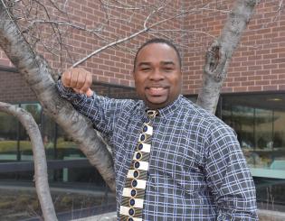 black man standing by a tree smiling