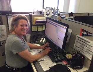 woman in a grey shirt at computer smiling