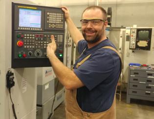 white male standing in front of a CNC maching smiling