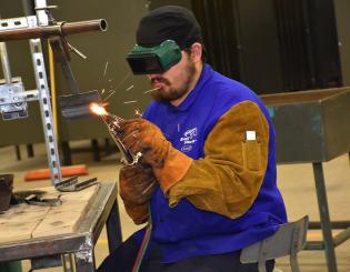 man welding while wearing protective goggles and gloves