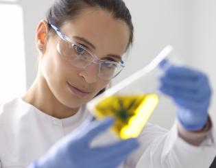 science student looking at a cannabis leaf inside a beaker