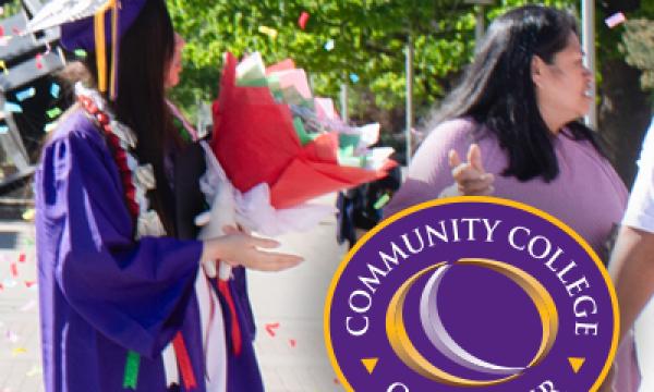 Student wearing purple commencement regalia and holding flowers. A woman wearing a purple shirt stands next to the student. 