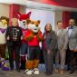 a group of seven people wearing business attire posing with three mascots; Swoop, Foxy, and Copper for the photo