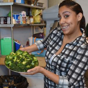 girl in plaid shirt shows off a bowl of broccoli