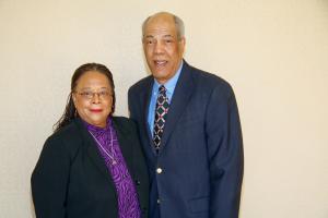 woman wearing purple and black next to a man in a blue suit and tie