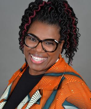 black woman wearing glasses in an orange shirt smiling
