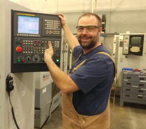 white male standing in front of a CNC maching smiling