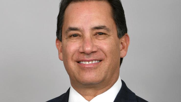 jim chavez smiling and wearing a blue blazer, white collared dress shirt, and light blue tie