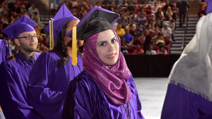 CCD graduate wearing purple cap and gown and fushia scarf standing in line to get her diploma