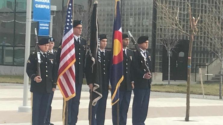 5 miliary men standing at attention in a row holding flags