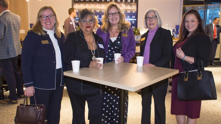 group of 5 women standing together at a table smiling