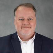 man with short brown hair and close cropped graying beard wearing navy blazer and white shirt