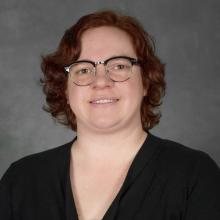 Woman with short wavy red hair wearing glasses and black sweater
