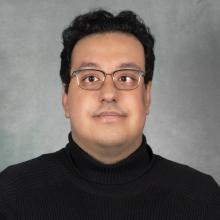 Man with short dark hair wearing glasses and a black turtleneck sweater