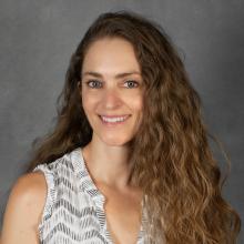 Woman with long brown wavy hair wearing a white print top