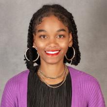 Woman with dark braided hair wearing hoop earrings and purple sweater with black top