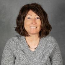Woman with chin length auburn hair wearing a gray v-neck sweater