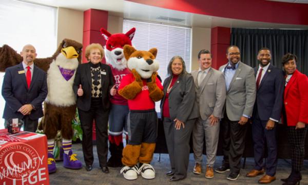 a group of seven people wearing business attire posing with three mascots; Swoop, Foxy, and Copper for the photo
