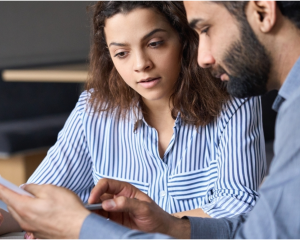 image of two people meeting and reading a paper. The women is in a striped shirt, while the bearded man is in a gray shirt 