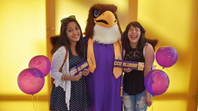 Two CCD Students holding an Alumni bumpersticker with the mascot