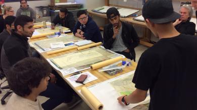 students around a design table with drafting designs